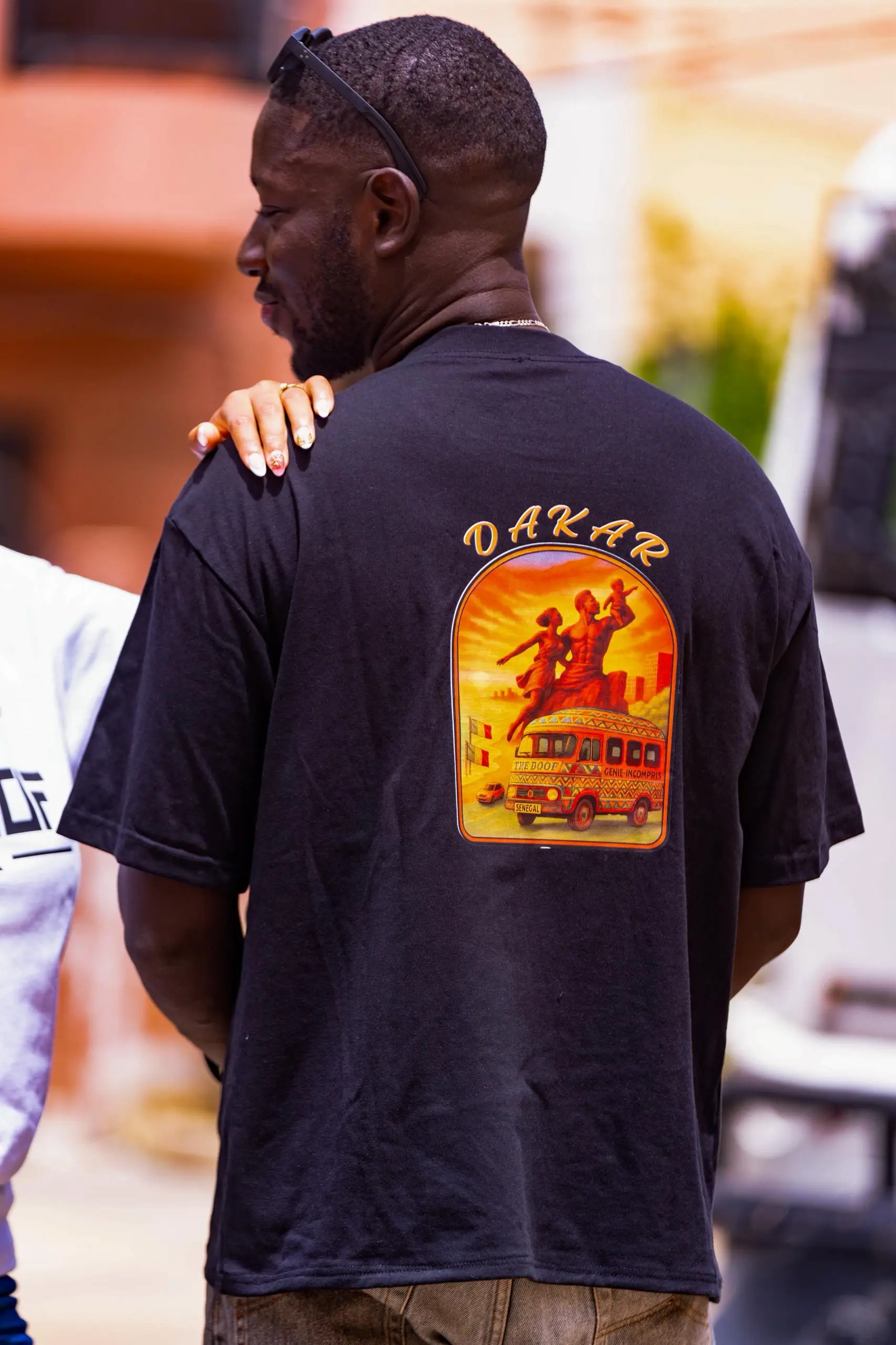 T-shirt streetwear Dakar DOOF_DKR - Allie style urbain sénégalais et identité culturelle. Au dos, une illustration unique du Monument de la Renaissance Africaine et d'un car rapide typique évoque l'âme de Dakar.